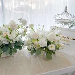 Two white floral arrangements on a table with a decorative birdcage