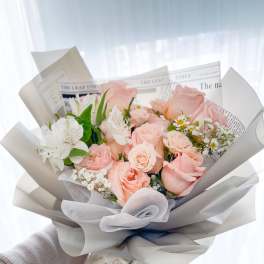 Hand-tied bouquet of pale pink roses and white flowers wrapped in gray paper