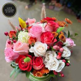 Mixed arrangement of pink, red and white roses with accent blooms in a green striped vase