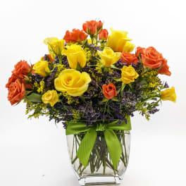 Yellow and orange roses in a clear glass vase with a green ribbon