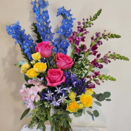 Colorful mixed bouquet in a clear glass vase with tall blue and purple blooms