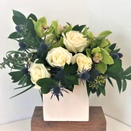 White roses and green orchids in a white square vase