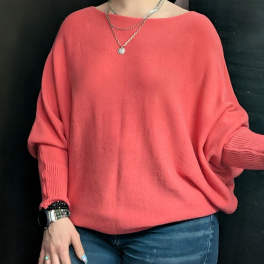Person wearing a coral oversized sweater with jeans and jewelry