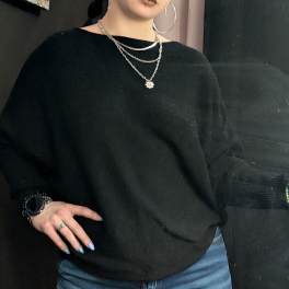 Person wearing a black sweater with layered silver necklaces and hoop earrings