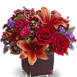 Red and purple floral arrangement in a square glass vase