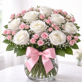 White and pink rose bouquet in a glass vase with a pink ribbon