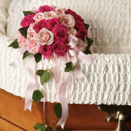 Pink and blush rose bouquet with ribbon streamers on a white casket