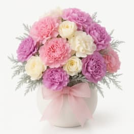 Pink, purple, and cream flowers arranged in a white vase with a pink ribbon.