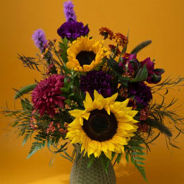 Bouquet with sunflowers and purple flowers in a textured vase