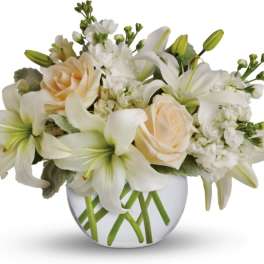 White lilies and cream roses arranged in a round glass vase