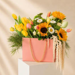Pink gift bag filled with yellow tulips, sunflowers, and daisies