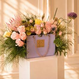 Lavender gift bag filled with pink and yellow roses and mixed blooms