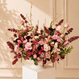 Large pink and burgundy floral arrangement in a white pedestal vase