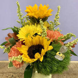 Sunflower and carnation arrangement in a white vase with a bee decoration