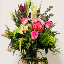 Tall mixed bouquet in a glass vase with pink lilies, roses, and a protea