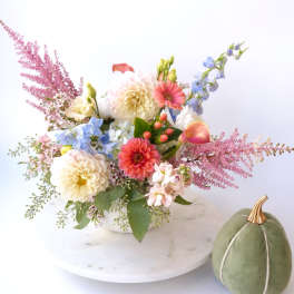 Mixed pastel flower arrangement in a white bowl with a green velvet pumpkin