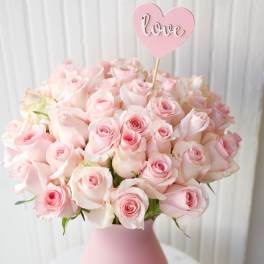 Pink rose bouquet in a matte pink vase with a heart-shaped love pick