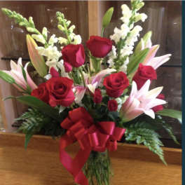 Bouquet of red roses and pink lilies in a glass vase with a red ribbon