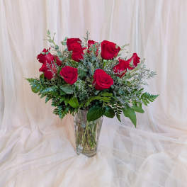 Red roses arranged in a clear glass vase with greenery