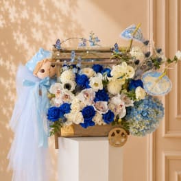 Blue and white floral arrangement in a wooden cart with a doll and lace umbrellas