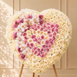 Heart-shaped floral arrangement of cream and pink roses with orchids on an easel