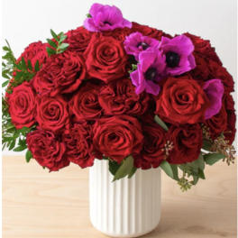Red roses and purple flowers arranged in a white vase