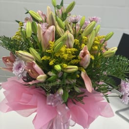 Pink lilies and daisies in a glass vase with pink wrapping