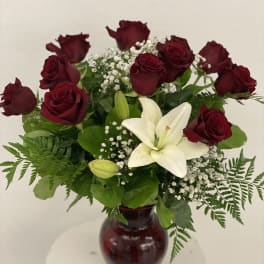 Red roses and a white lily arranged in a burgundy vase