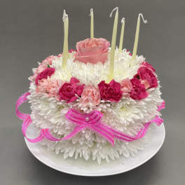 Round floral cake of white mums with pink roses, carnations, and tall candles on a plate