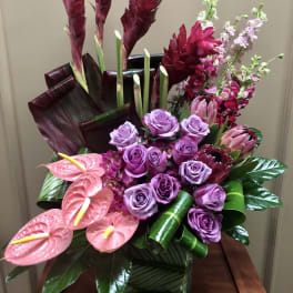Pink and purple tropical floral arrangement in a square vase