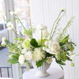 White floral arrangement in a white urn vase on a round pedestal