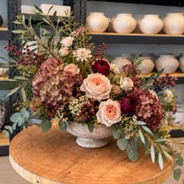 Mixed bouquet in a stone pedestal bowl with pink and burgundy blooms