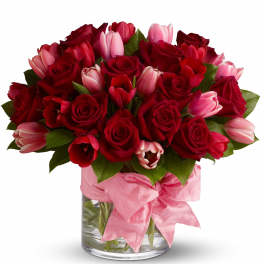 Red roses and pink tulips in a glass vase with a pink ribbon