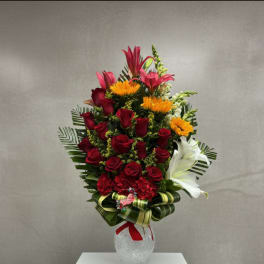 Tall bouquet of red roses, lilies, and yellow flowers in a glass vase