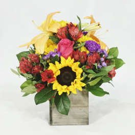 Mixed bouquet with a sunflower, pink rose, and yellow lilies in a wooden box