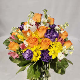 Mixed bouquet of orange roses, purple carnations, and yellow daisies in a glass vase