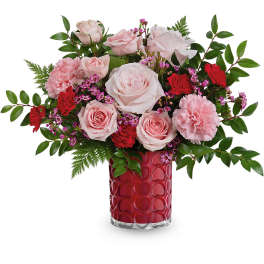Pink roses and carnations arranged in a red glass vase