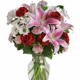Bouquet of pink lilies, red roses, white daisies, and carnations in a glass vase