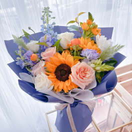 Bouquet of sunflowers, roses, and pastel flowers wrapped in blue paper
