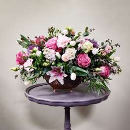 Pink and white mixed flower arrangement in a brown bowl on a purple stand