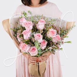 Large bouquet of light pink roses with small pink filler flowers wrapped in kraft and tissue paper