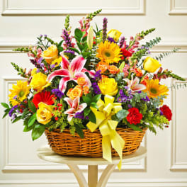 Bright mixed basket with yellow roses, pink lilies, red carnations and other flowers with a yellow bow