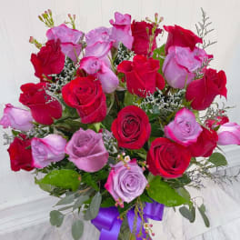 Arrangement of red and lavender roses in a clear vase with a purple ribbon bow