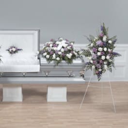 Funeral casket surrounded by white and purple floral sprays