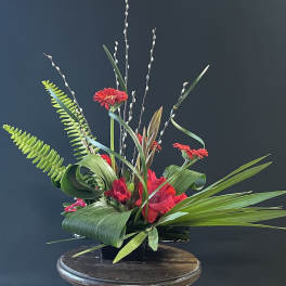 Red gerbera daisies in a black container with tall willow branches