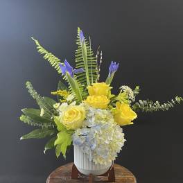 Yellow roses and blue hydrangea in a white vase with tall purple iris