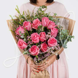 Bouquet of bright pink roses with tiny pink filler flowers wrapped in kraft paper, held by a person in a pale dress.
