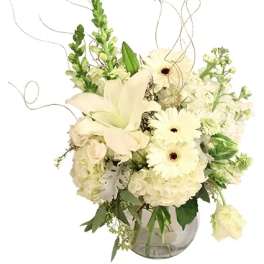 White floral arrangement in a glass vase with lilies and daisies