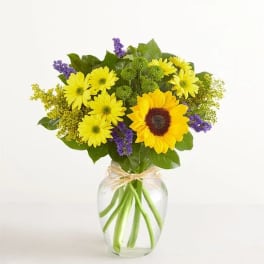 Yellow daisies and a sunflower in a clear glass vase