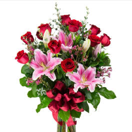 Bouquet of red roses and pink lilies in a glass vase with a red ribbon